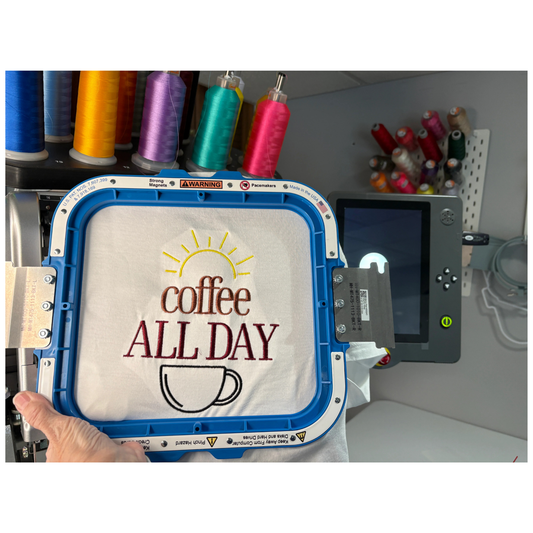 Embroidery design with 'coffee ALL DAY' text on a white shirt and a line drawing of a sun and coffee mug