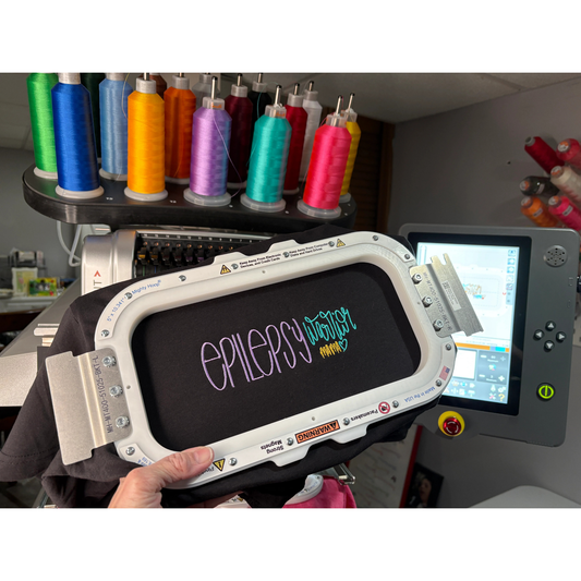 Embroidered tshirt in a hoop that says epilepsy warrior in front of an embroidery machine