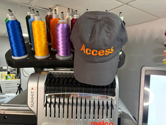 Gray cap with 'Access' text on a machine with spools of colorful thread.