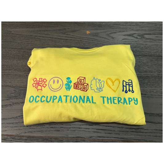 Yellow sweatshirt with colorful icons and 'Occupational Therapy' text on a wooden surface