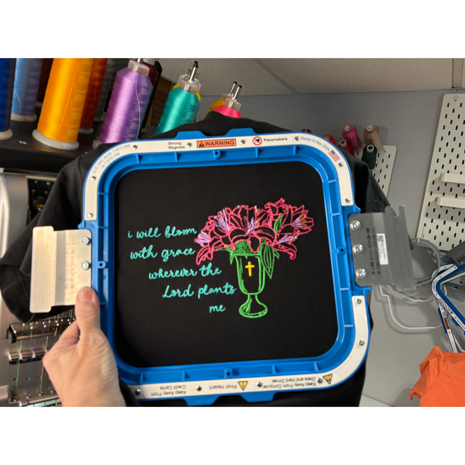 a black embroidered tshirt with flowers in a vase and the words I will bloom with grace wherever the lord plants me