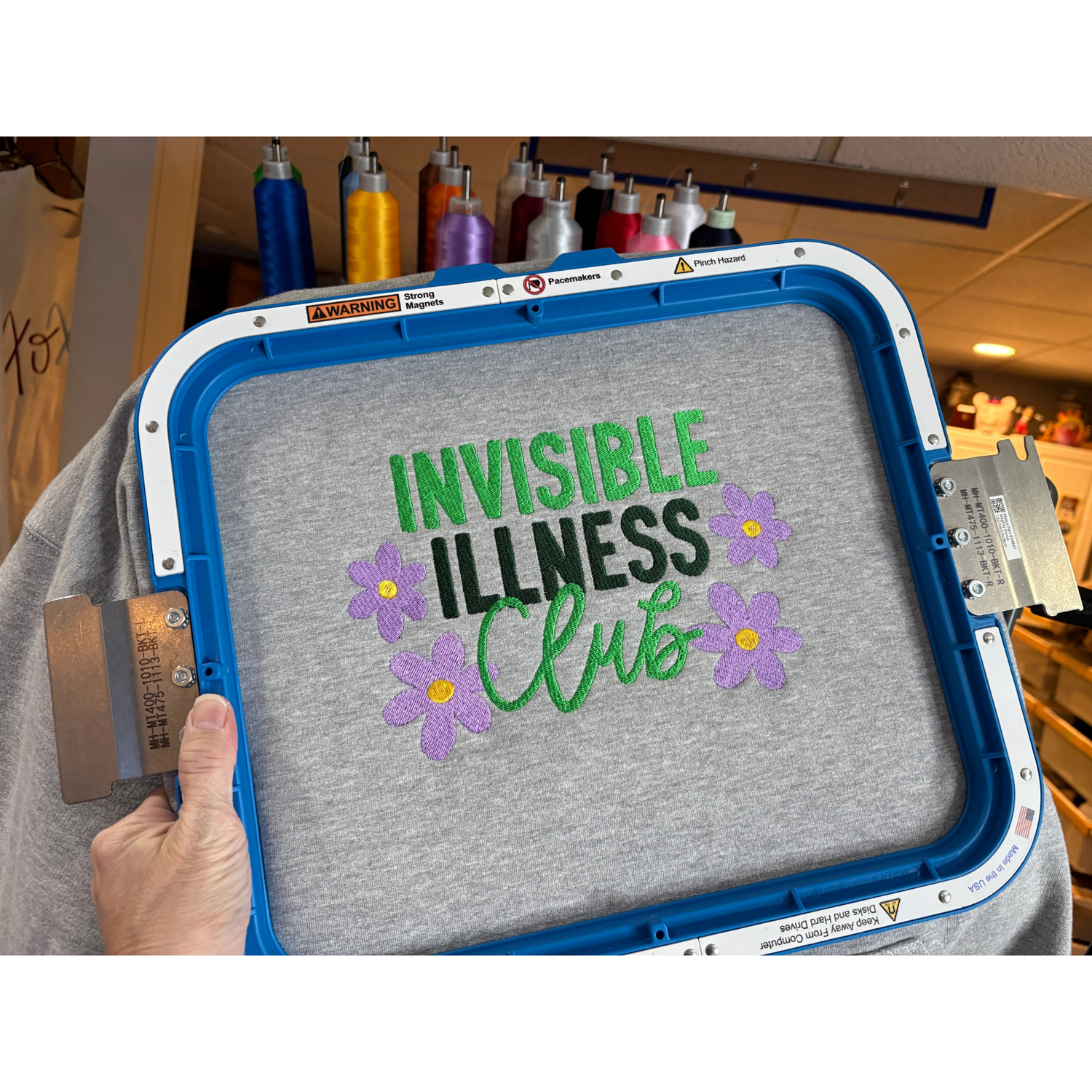 Gray sweatshirt embroidered Invisible Illness Club with purple flowers