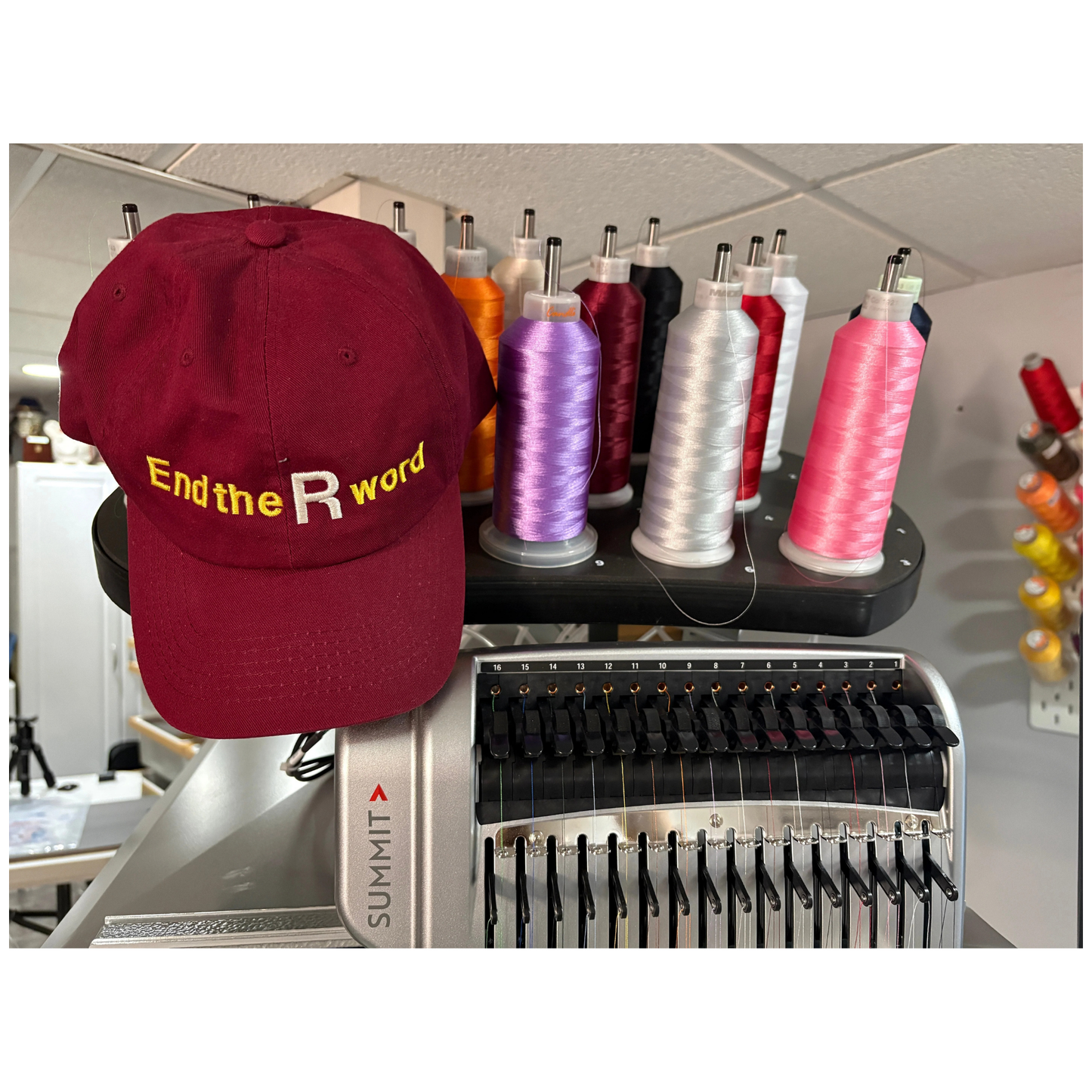Maroon cap with 'End the R word' text on a machine with spools of thread.