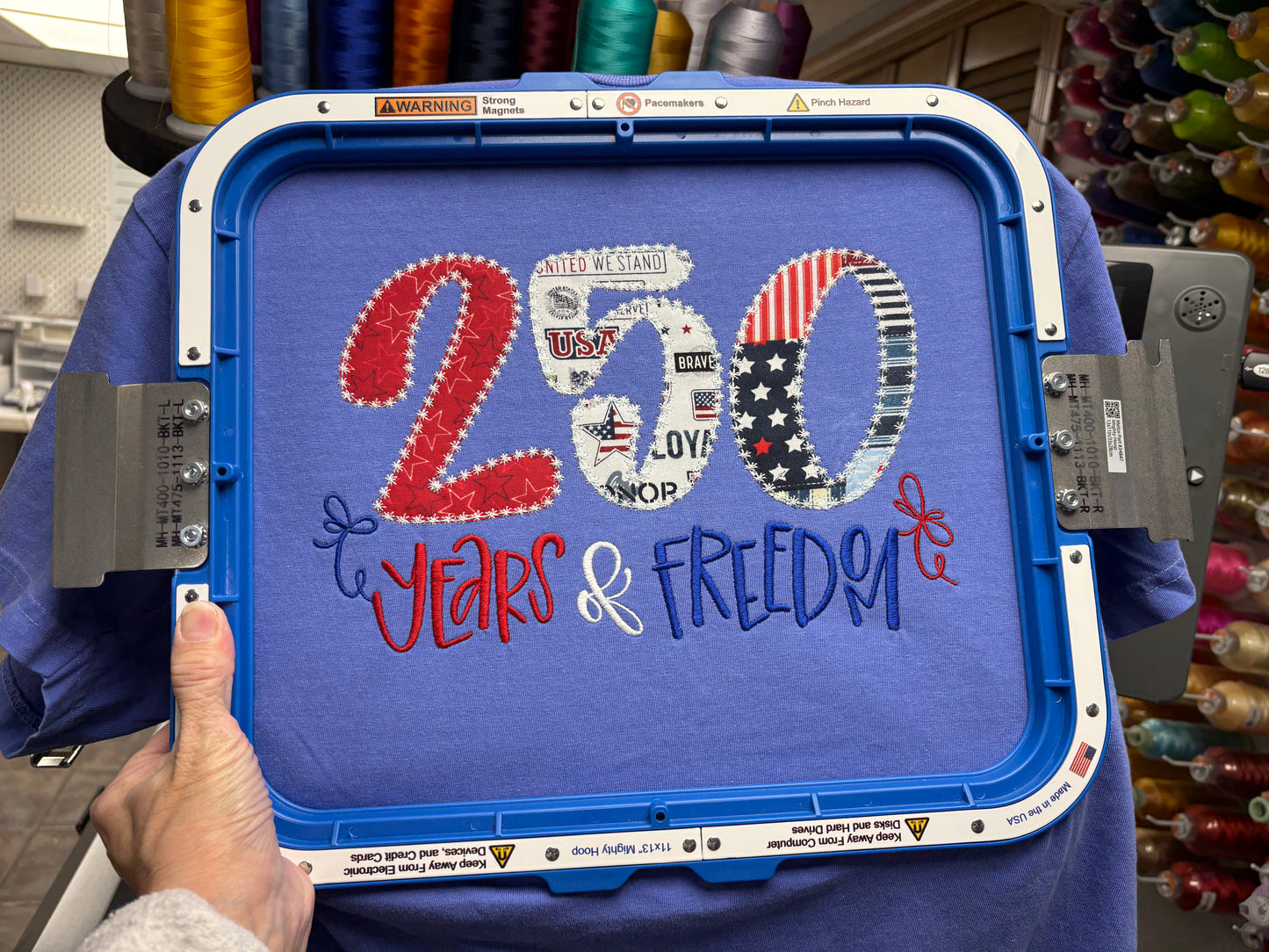 Blue embroidery machine hoop with '200 Years & Freedom' text and American flag design.