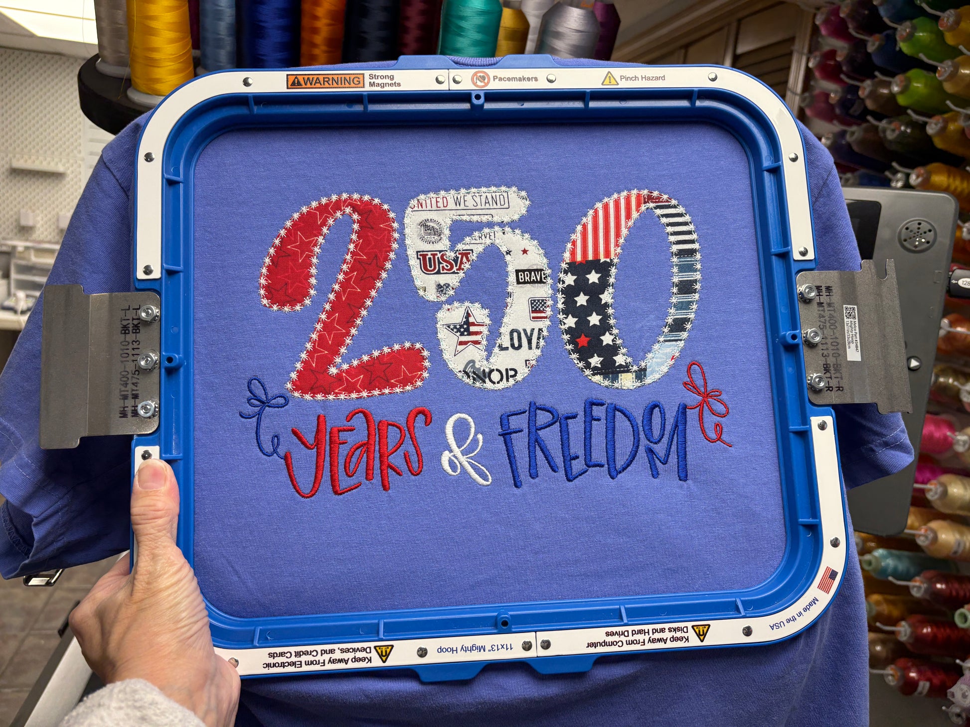 Blue embroidery machine hoop with '200 Years & Freedom' text and American flag design.