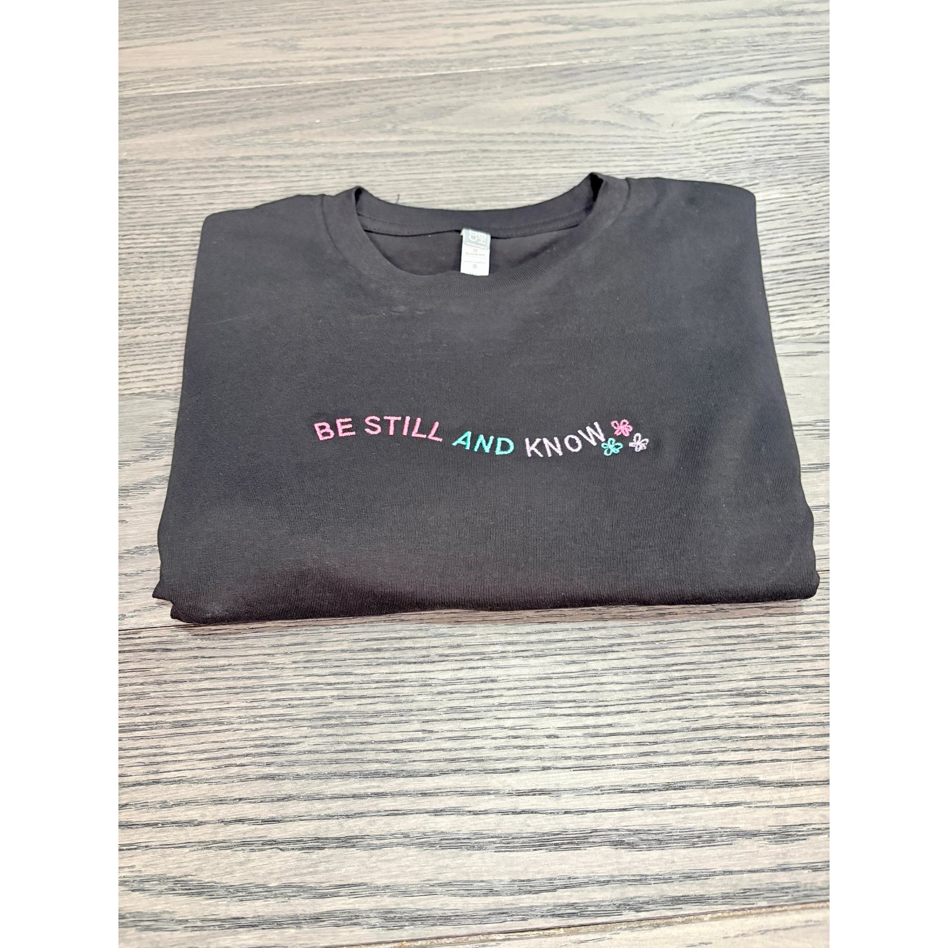 Embroidered black shirt that reads Be Still and Know