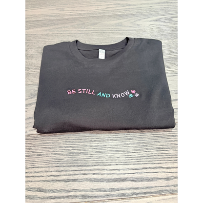 Embroidered black shirt that reads Be Still and Know