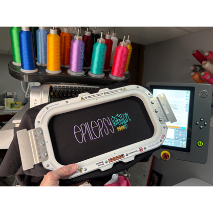 Embroidered tshirt in a hoop that says epilepsy warrior in front of an embroidery machine 