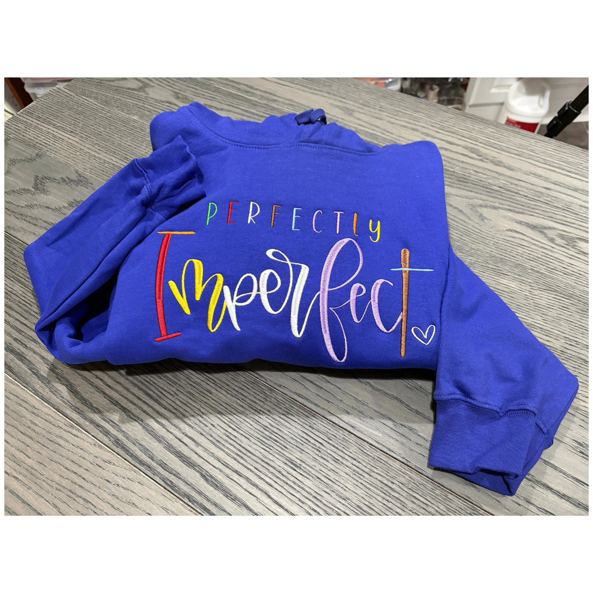 Blue sweatshirt with 'Perfectly Imperfect' text on a wooden surface