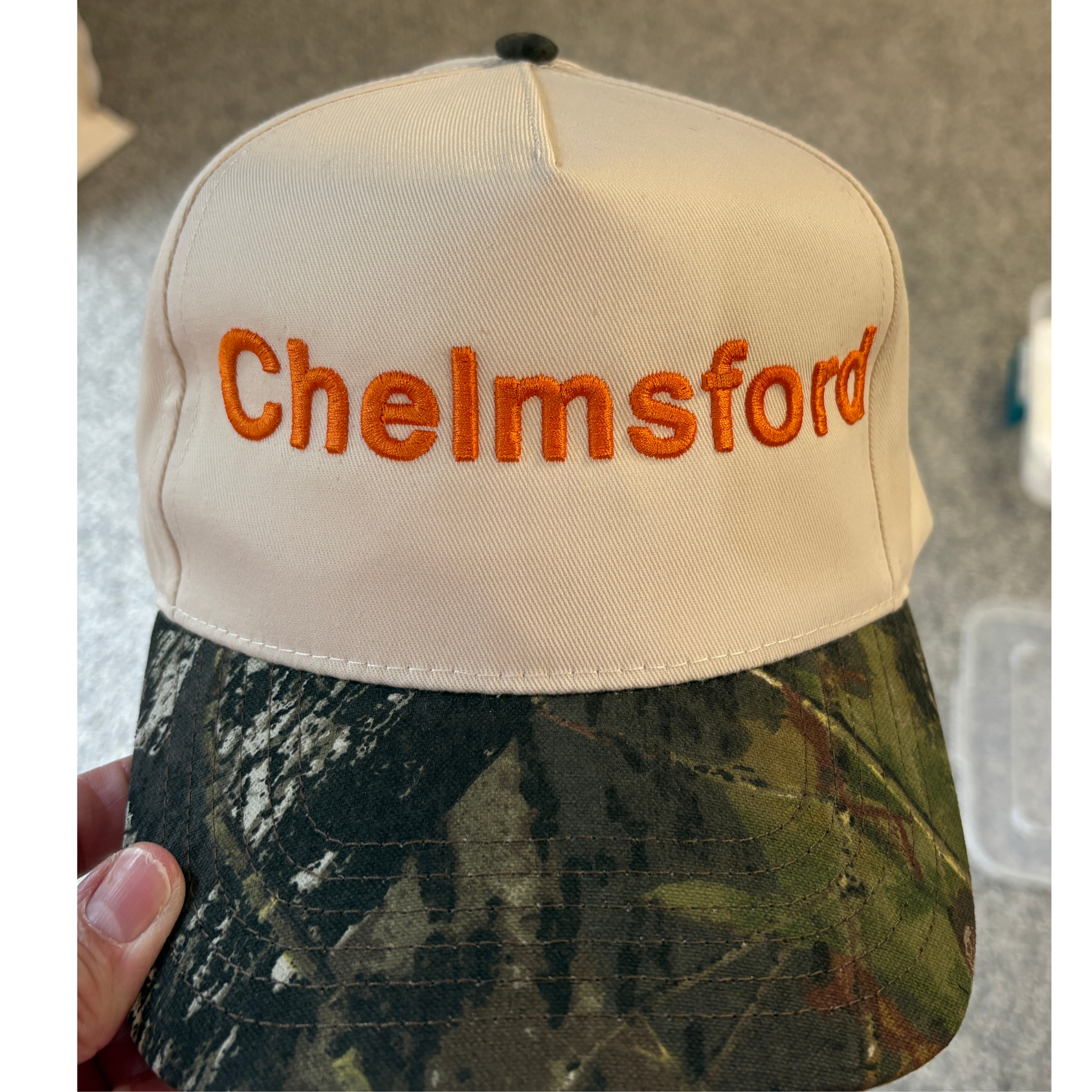 Chelmsford Text in Orange on a camo hat and natural hat