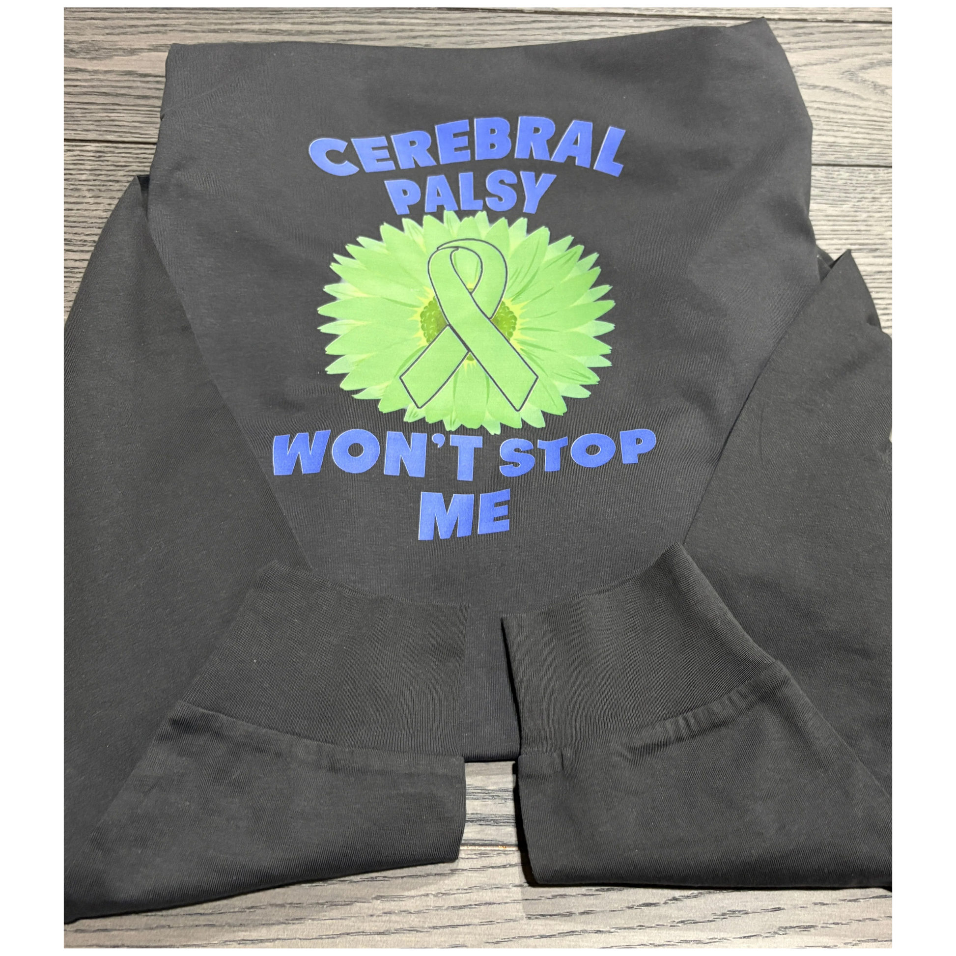 Dark gray shirt with a green ribbon, greee flower,  and text saying Cerebral Palsy won't stop me. 