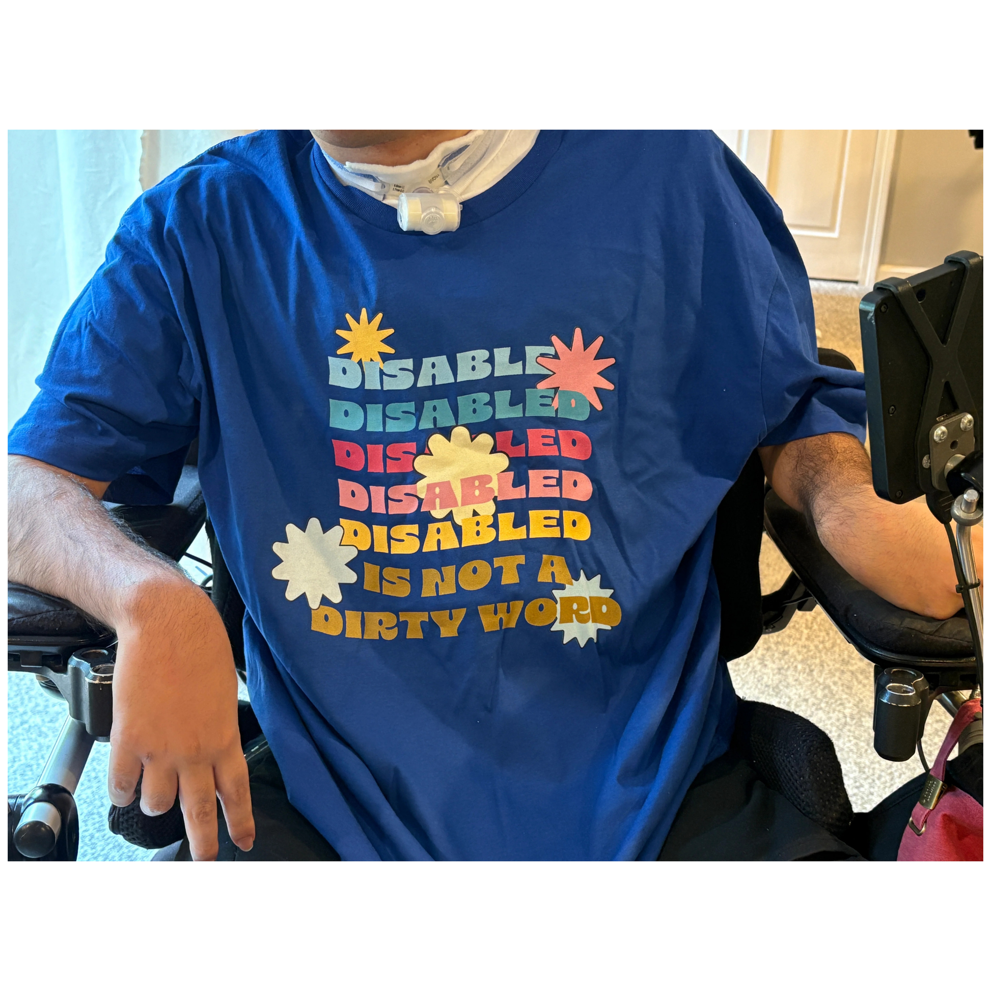 Person wearing a blue shirt with colorful text in a wheelchair.