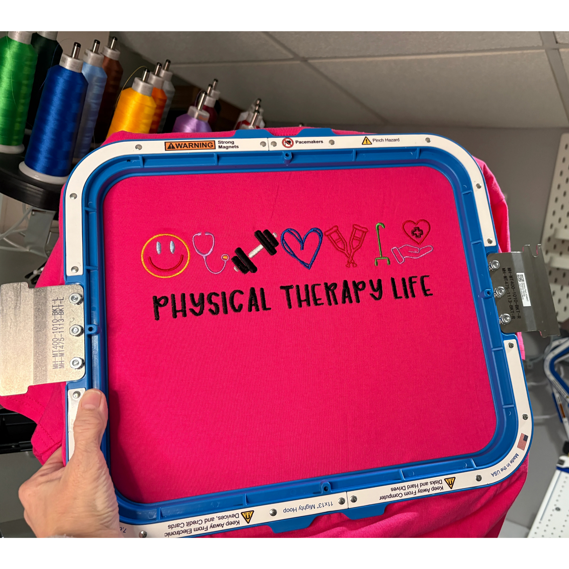 Pink embroidered sweatshirt inside a hoop with 'physical therapy life' text and symbols