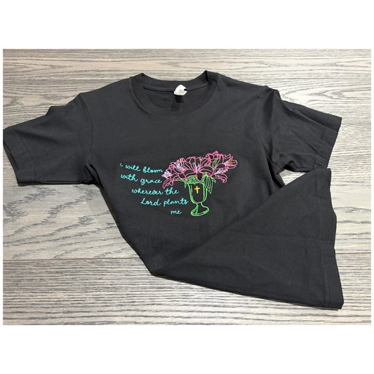 Black t-shirt with flowers in a vase and text saying I will bloom with grace wherever the lord plants me.
