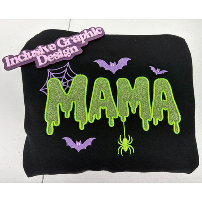 A black sweatshirt applique featuring a Halloween-themed  'MAMA' design in dripping neon green glitter-style lettering, purple bats, a spider, and a spiderweb, shown on a white background with a purple 'Inclusive Graphic Design' brand marker