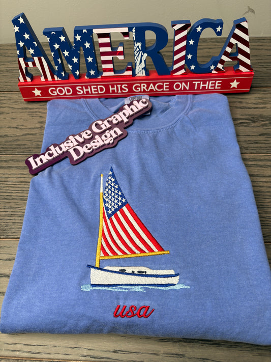 Blue t-shirt with American flag sailboat design and USA text on a wooden surface