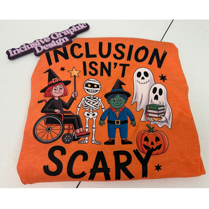 An orange graphic T-shirt with the phrase 'INCLUSION ISN'T SCARY' in large black letters with Halloween characters including a witch in a wheelchair, a skeleton, a child wizard, 2 ghosts, and a pumpkin. A brand marker reading 'Inclusive Graphic Design' is at the top left.