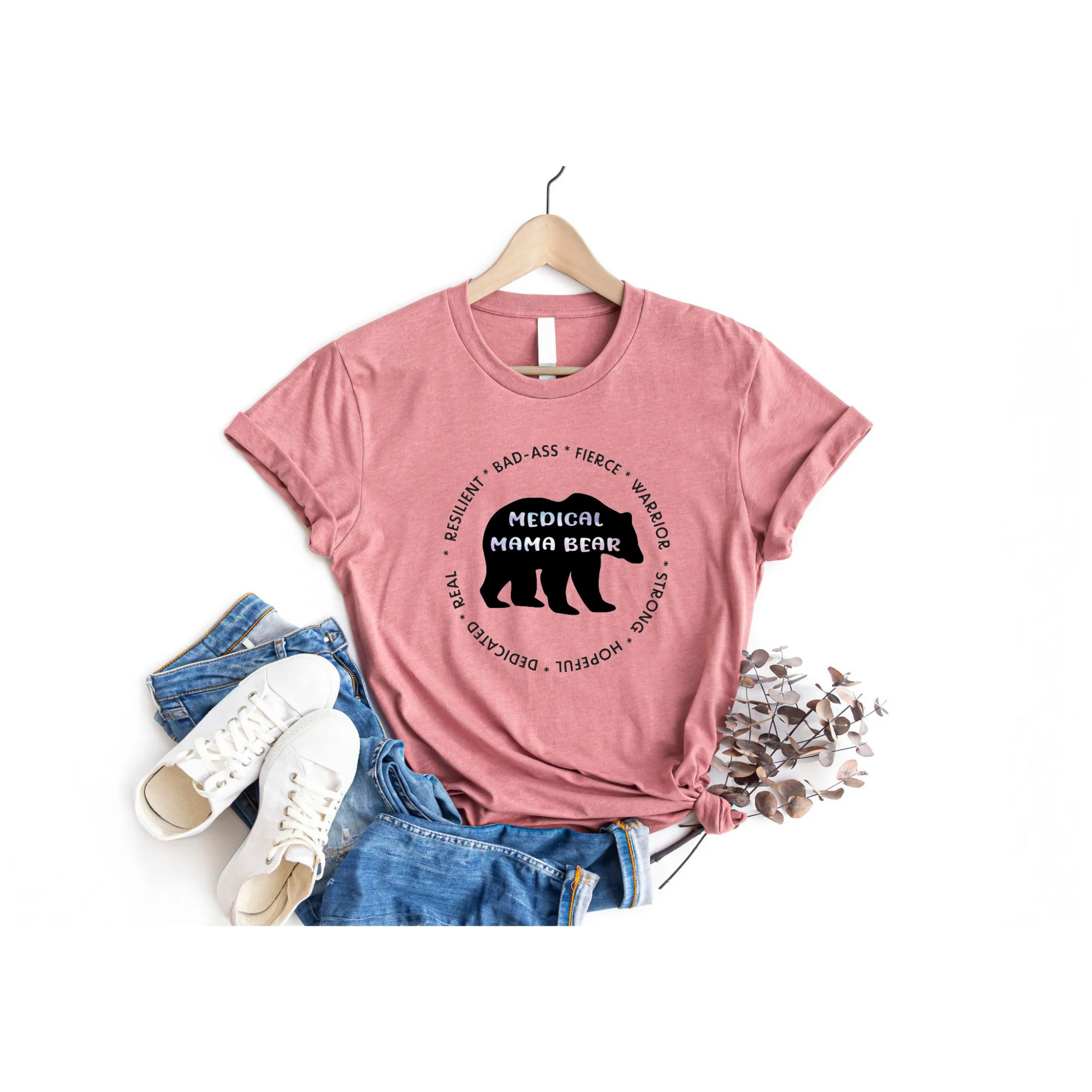 Pink t-shirt with 'Medical Mama Bear' graphic on a hanger with jeans and sneakers below.