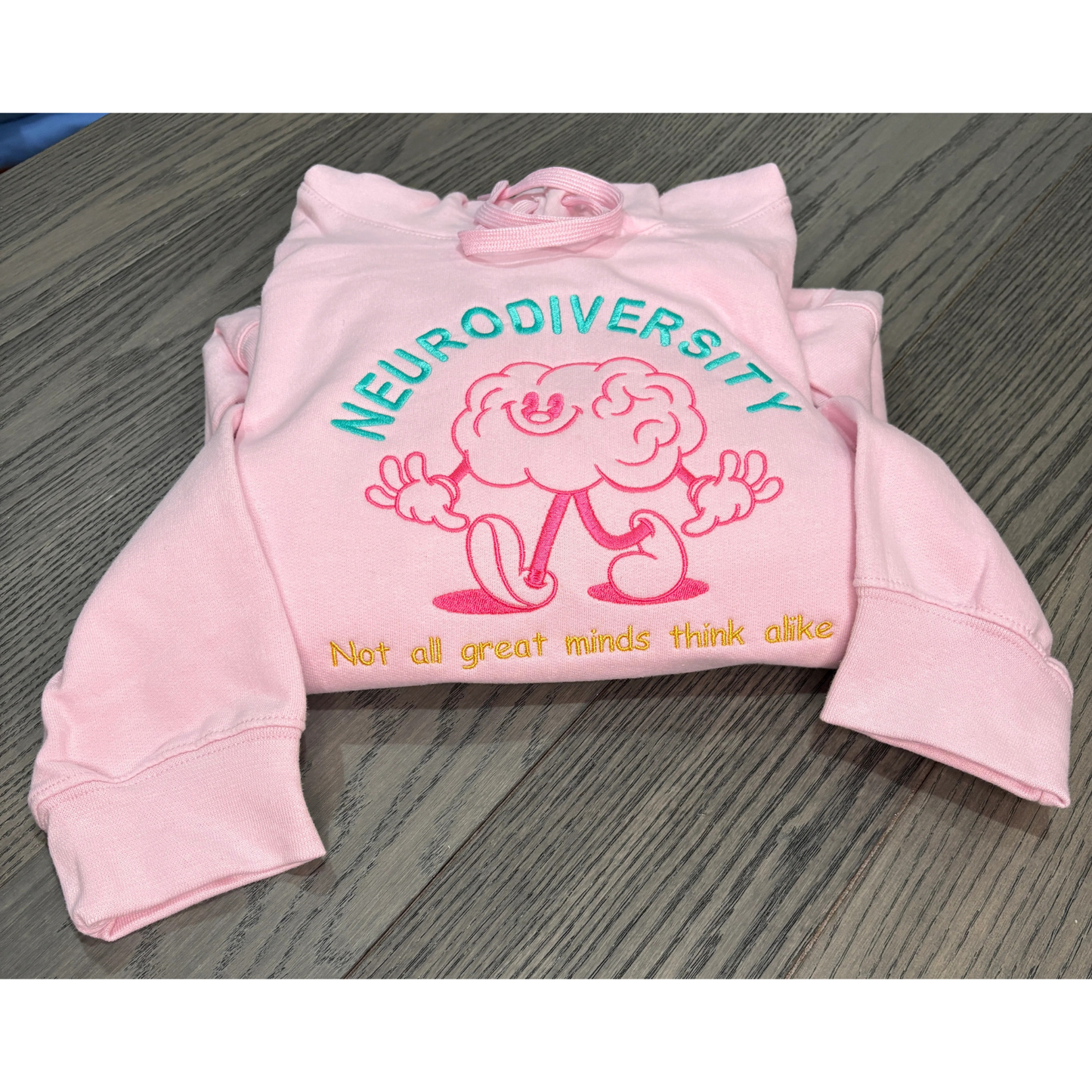 Pink sweatshirt in teal, fascia, and gold emebroidered thread that reads Neurodiversity Not all great minds think alike 
