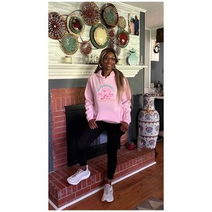 Woman in a pink hoodie standing in front of a fireplace wearing a pink embroidered hoodie that says Neurodiversity not all great minds think alike. 