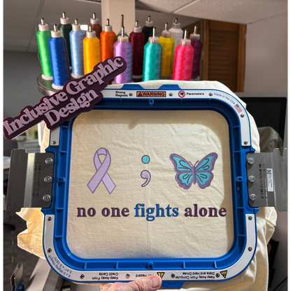 Embroidery hoop with a design of a ribbon, semicolon, and butterfly with text 'no one fights alone'.