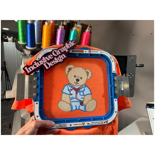 Embroidery hoop with a teddy bear design on an orange fabric, surrounded by spools of thread.