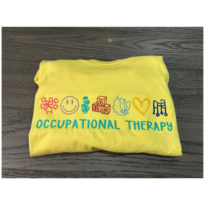 Yellow sweatshirt with colorful icons and 'Occupational Therapy' text on a wooden surface