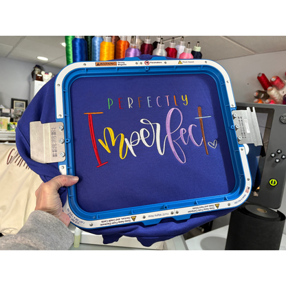 Blue sweatshirt with Perfectly Imperfect embroidered in different bright colors.