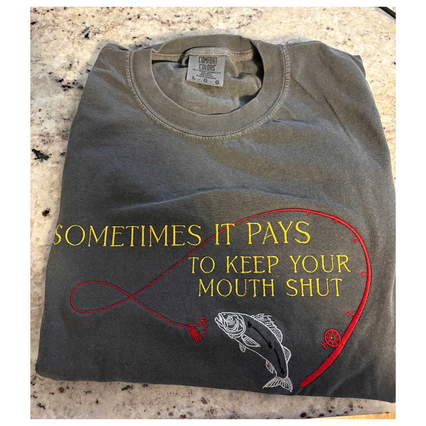 Folded t-shirt with fishing-themed design and text on a textured surface