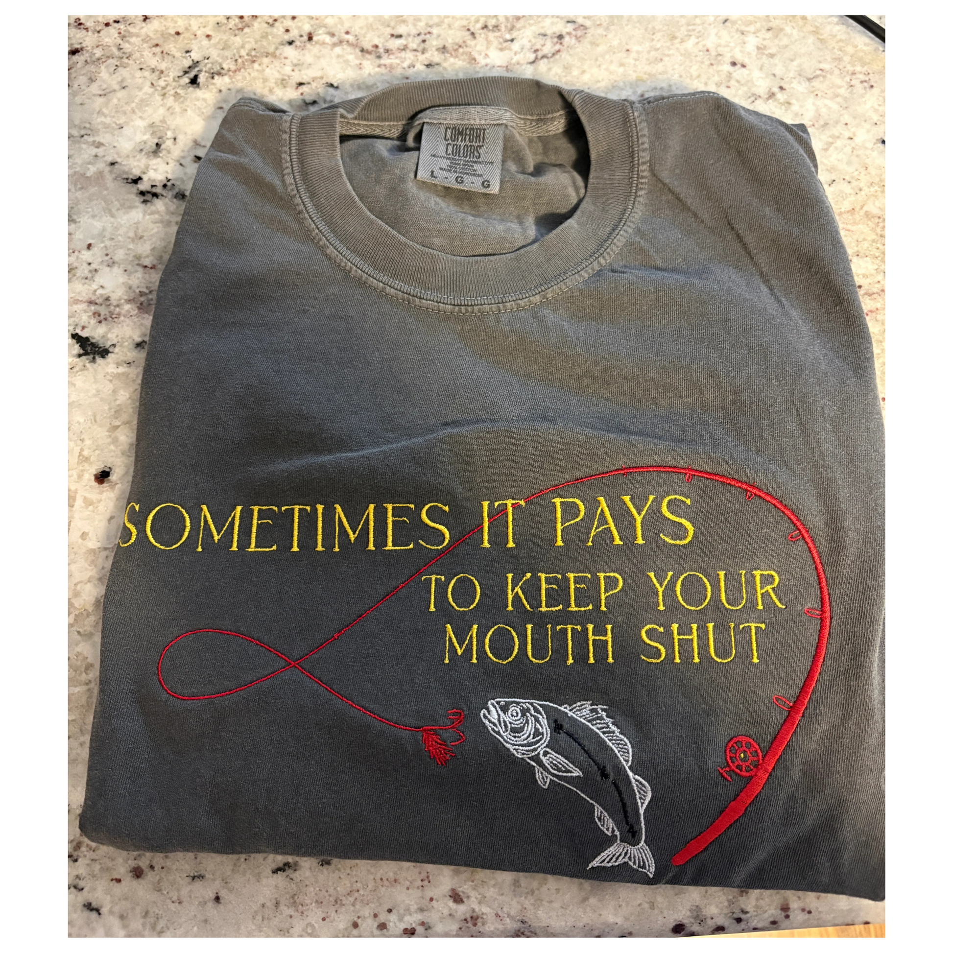 Folded t-shirt with fishing-themed design and text on a textured surface