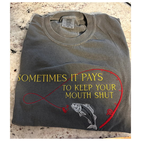 Folded t-shirt with fishing-themed design and text on a textured surface