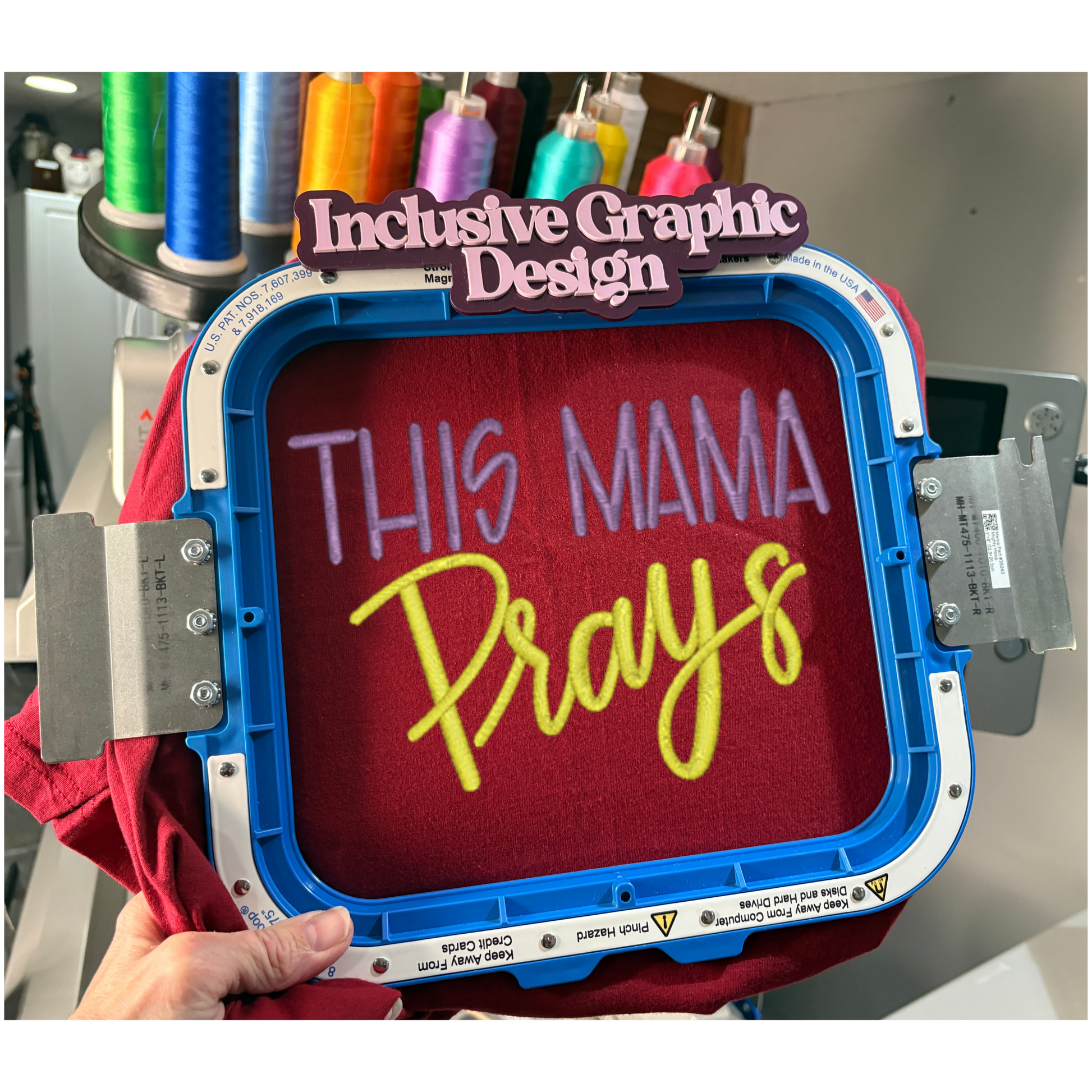 Embroidery hoop with 'This Mama Prays' text on a red fabric, surrounded by spools of thread.