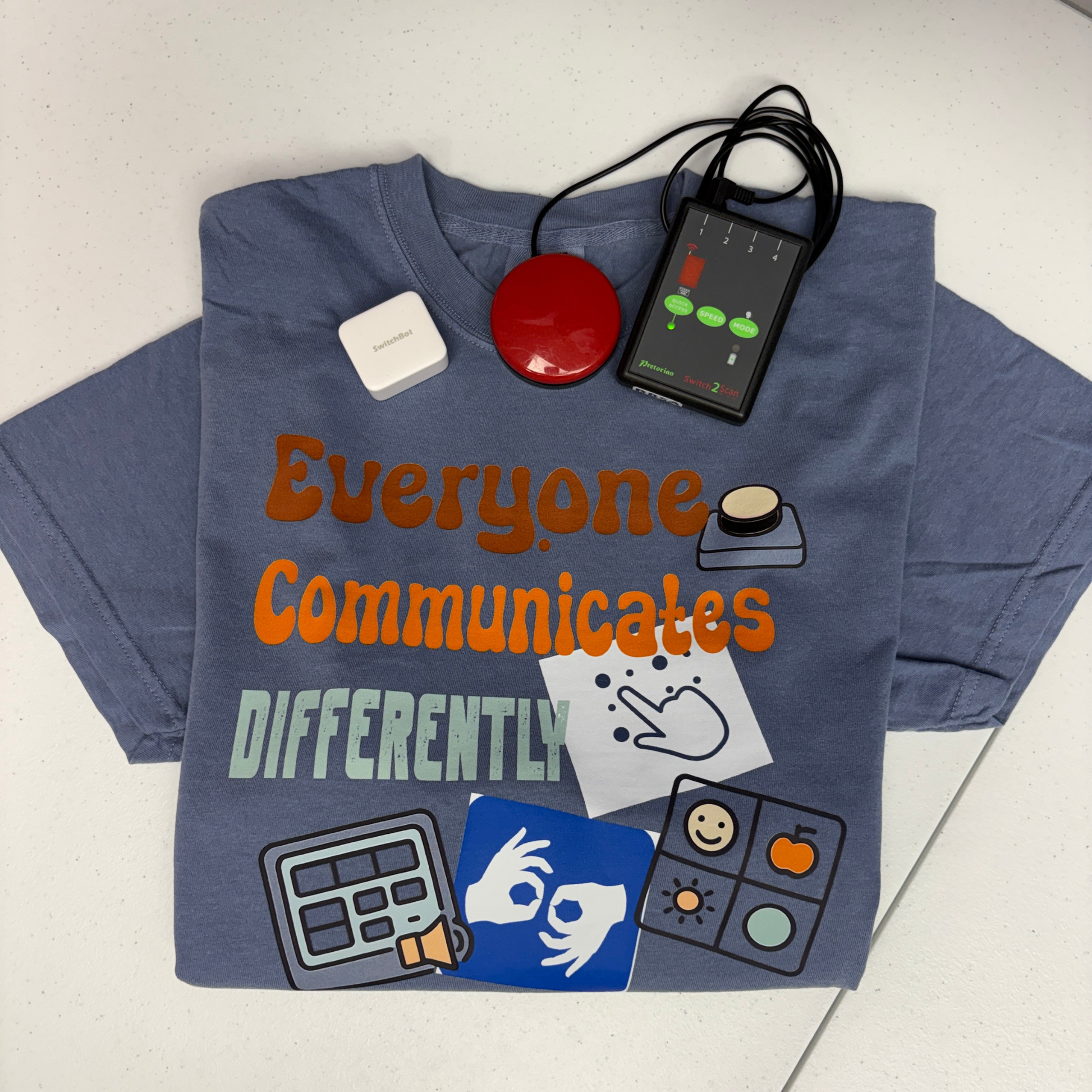 Blue t-shirt with communication aids and text 'Everyone Communicates DIFFERENTLY' on a white background