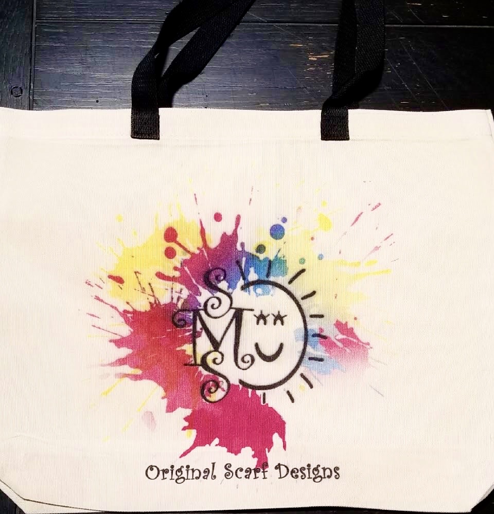 off-white tote bag with black handles and a logo with the initials S.M.S. written vertical to the left of a sun symbol and splashes of color.